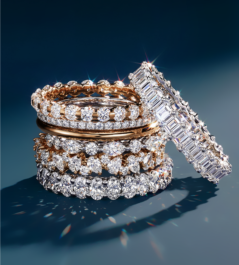 A stack of five diamond-studded rings in rose and white gold set against a dark blue background, sparkling brightly, conveying elegance and luxury.