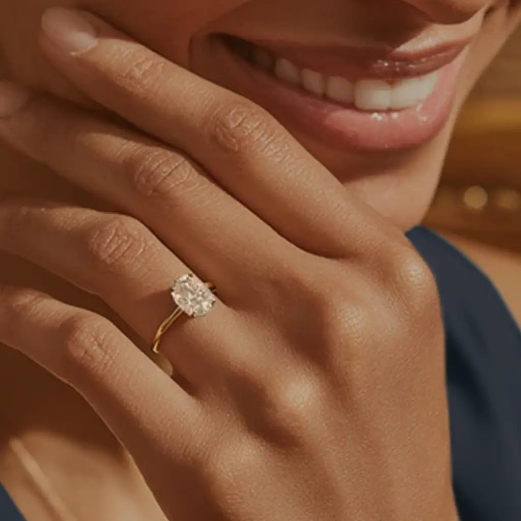 woman wearing a classic oval diamond solitaire engagement ring in yellow gold, hand resting gracefully near her face
