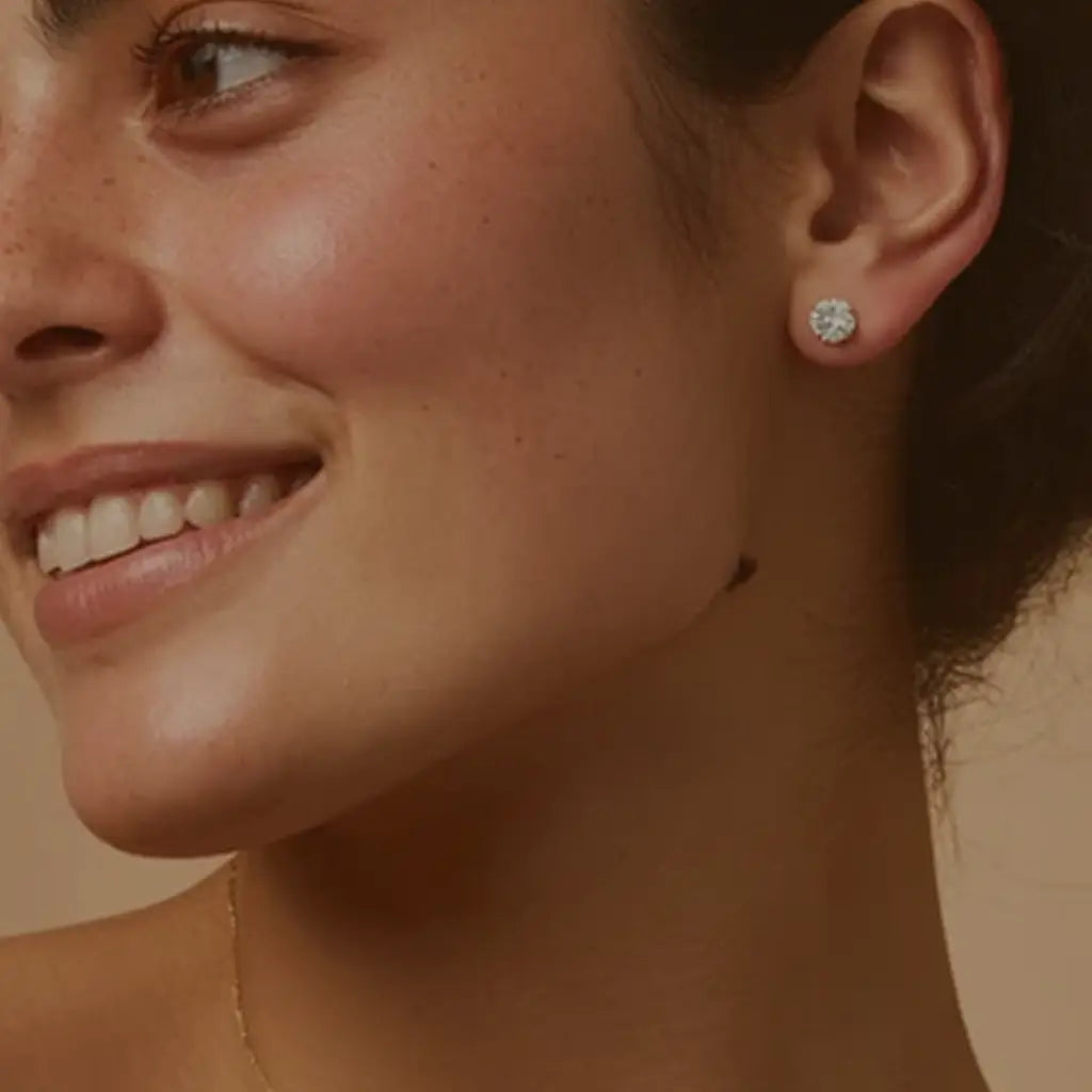 Smiling woman wearing round diamond stud earrings, hair tied back, showcasing the jewelry against a neutral background