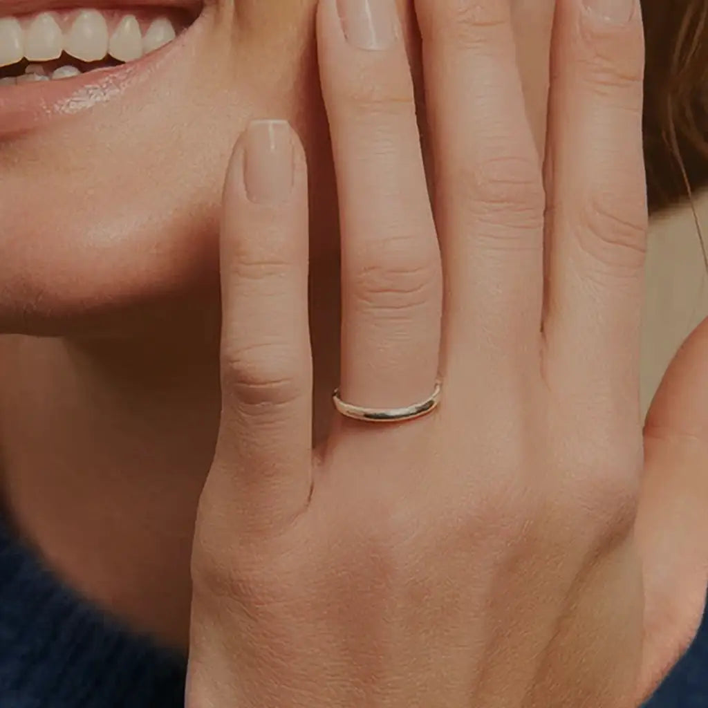 Smiling woman wearing a simple 3mm white gold wedding band, hand gently resting on her face