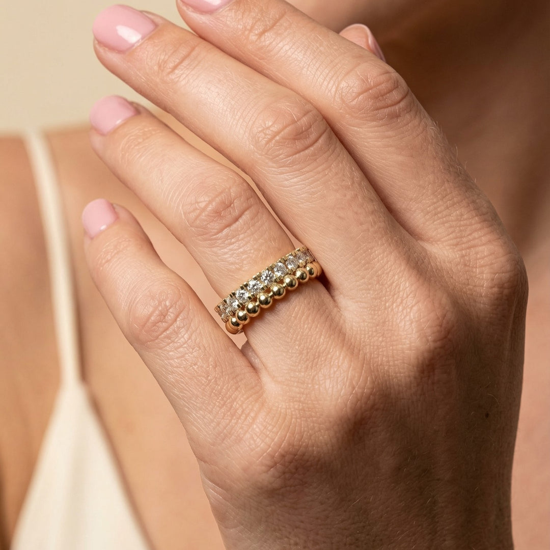 Close-up of a hand wearing a gold ring with diamonds on a neutral background