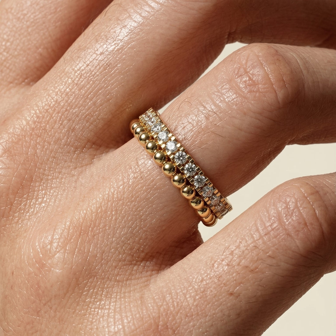 Gold and diamond ring on a person's finger against a neutral background