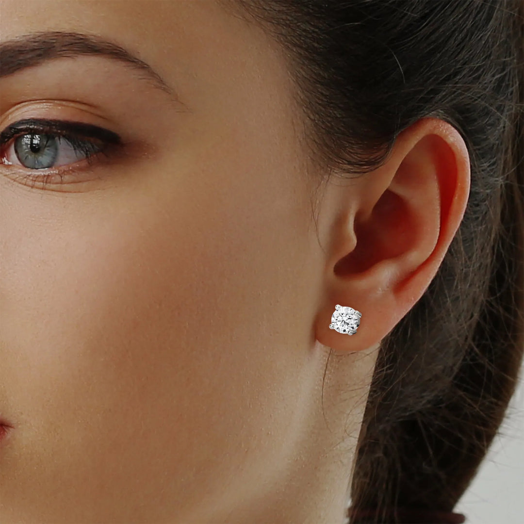 Close up of a diamond earring on an ear with dark hair visible.