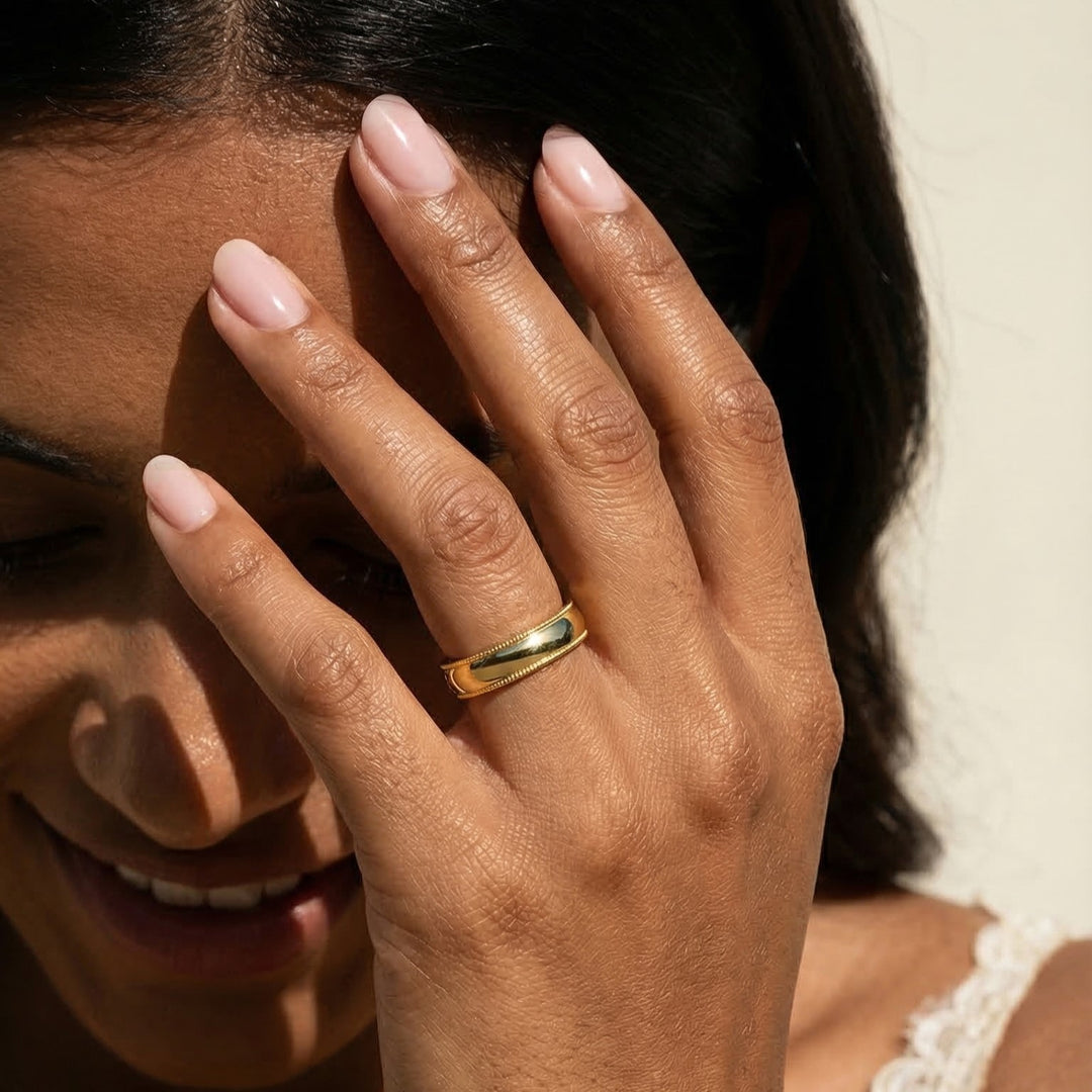Close-up of a hand with a gold ring covering part of a face, on a neutral background