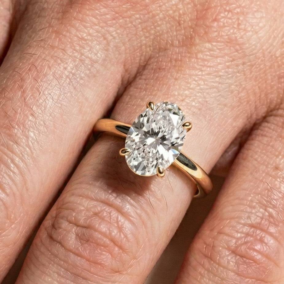 A close-up of a hand wearing a gold ring with a large, oval-cut diamond. The ring sits on the ring finger, showcasing elegance and luxury.