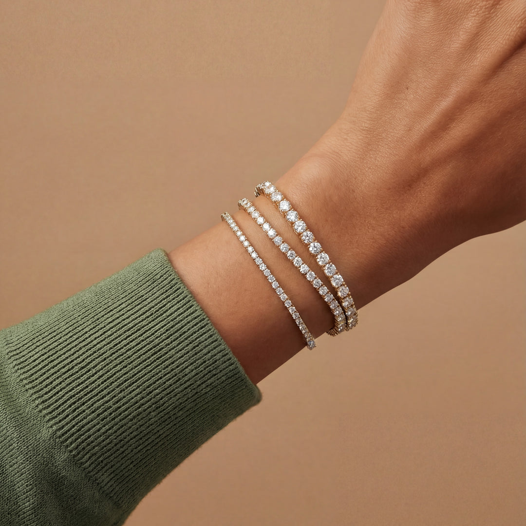 Close-up of a wrist wearing multiple diamond bracelets on a beige background