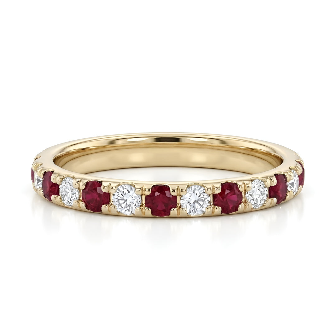 A gold band ring featuring alternating red rubies and white diamonds, creating a strikingly elegant and luxurious look on a reflective surface.