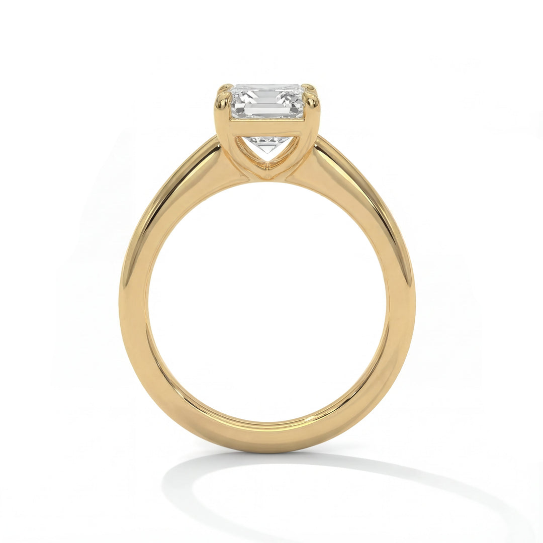 A gold engagement ring features a rectangular-cut diamond in a minimalist setting. The background is white, highlighting the ring's elegance and simplicity.