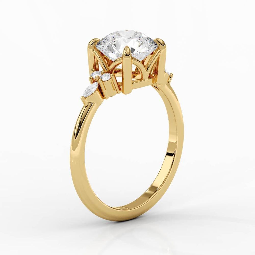 A gold engagement ring with a large round diamond centerpiece, flanked by smaller pear-shaped diamonds on either side, set against a white background.