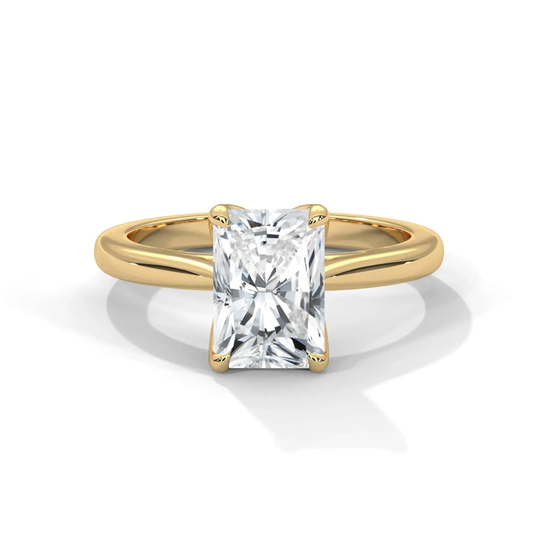 A gold engagement ring with a radiant-cut diamond set in a prong setting. The ring is elegant and shiny, casting a soft shadow on a white background.