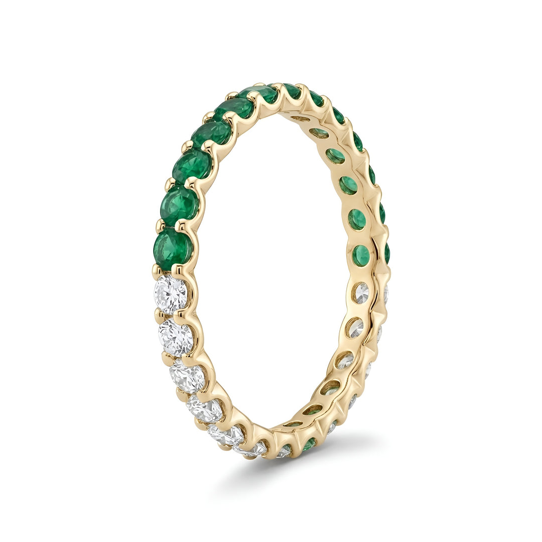A gold eternity ring featuring alternating green emeralds and clear diamonds, set against a white background. It conveys elegance and luxury.