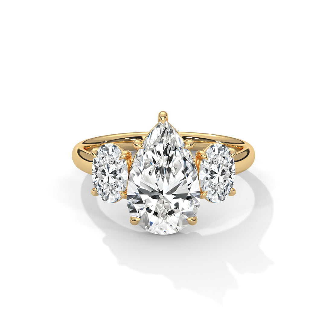 A gold ring features a large pear-shaped diamond in the center, flanked by two oval diamonds. The setting exudes elegance and luxury against a white background.