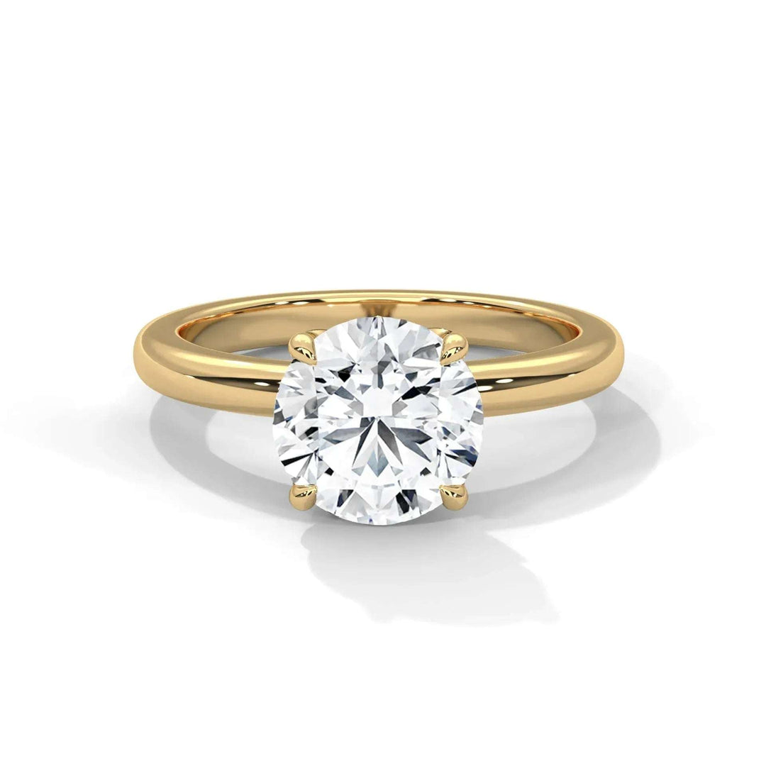 A gold ring features a solitaire round diamond in a four-prong setting. The diamond's brilliance contrasts with the simple, elegant gold band.