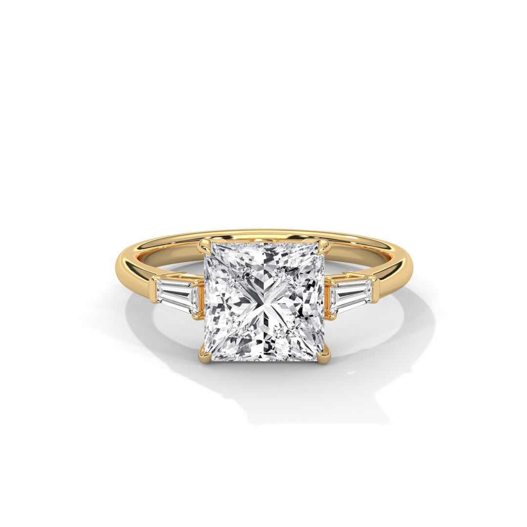 A gold ring featuring a large, square-cut diamond in the center, flanked by two smaller baguette diamonds. The setting is sleek and elegant.