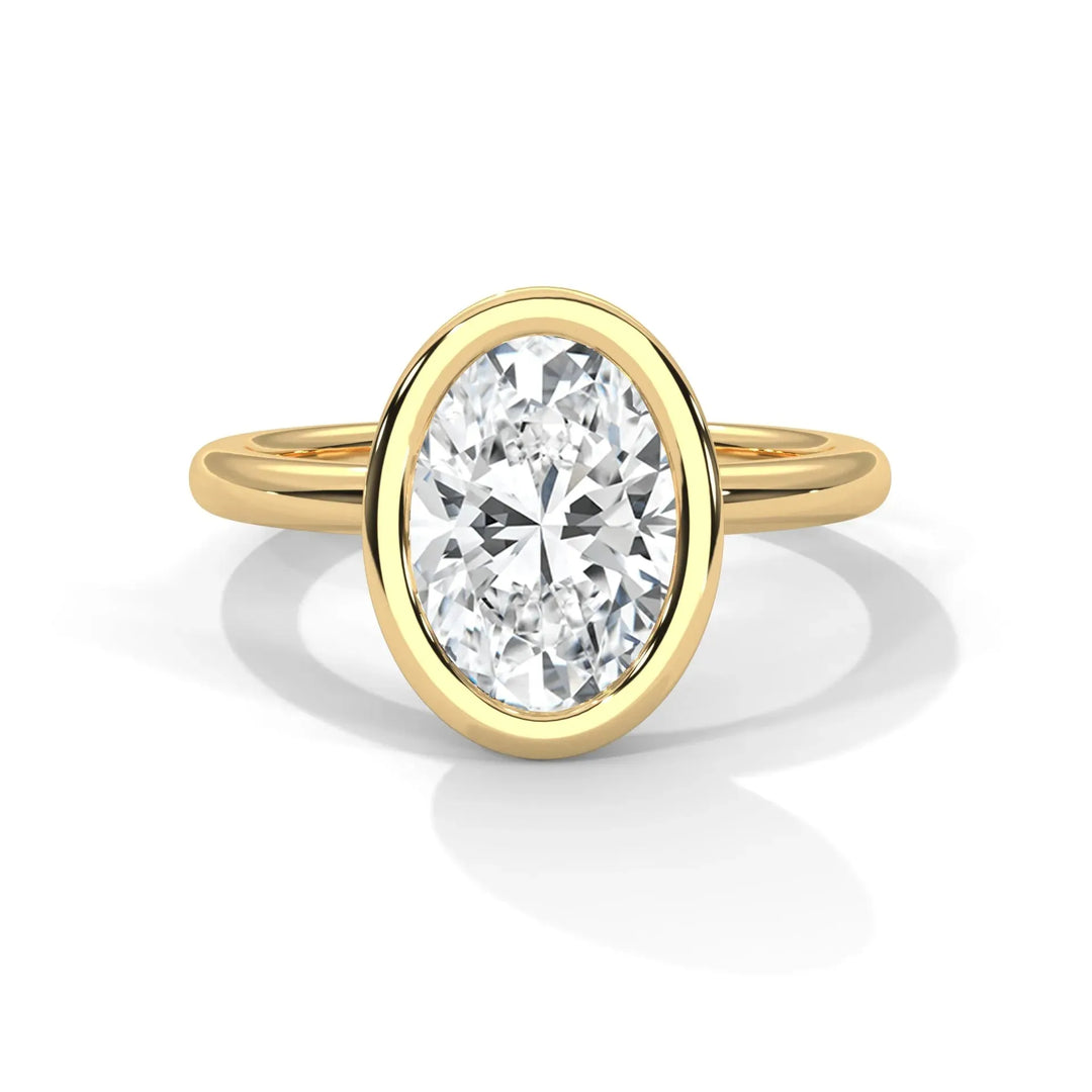 A gold ring with an oval-cut diamond in a bezel setting is centered on a white background. The diamond sparkles, conveying elegance and luxury.