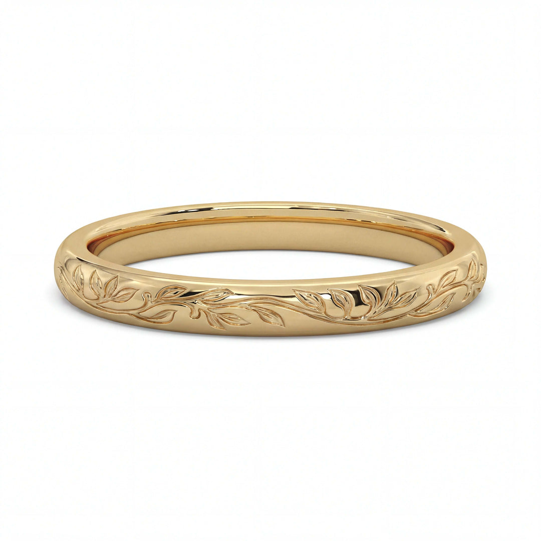 A gold ring with a polished finish features an engraved vine and leaf pattern. The design is delicate, creating an elegant and timeless look.
