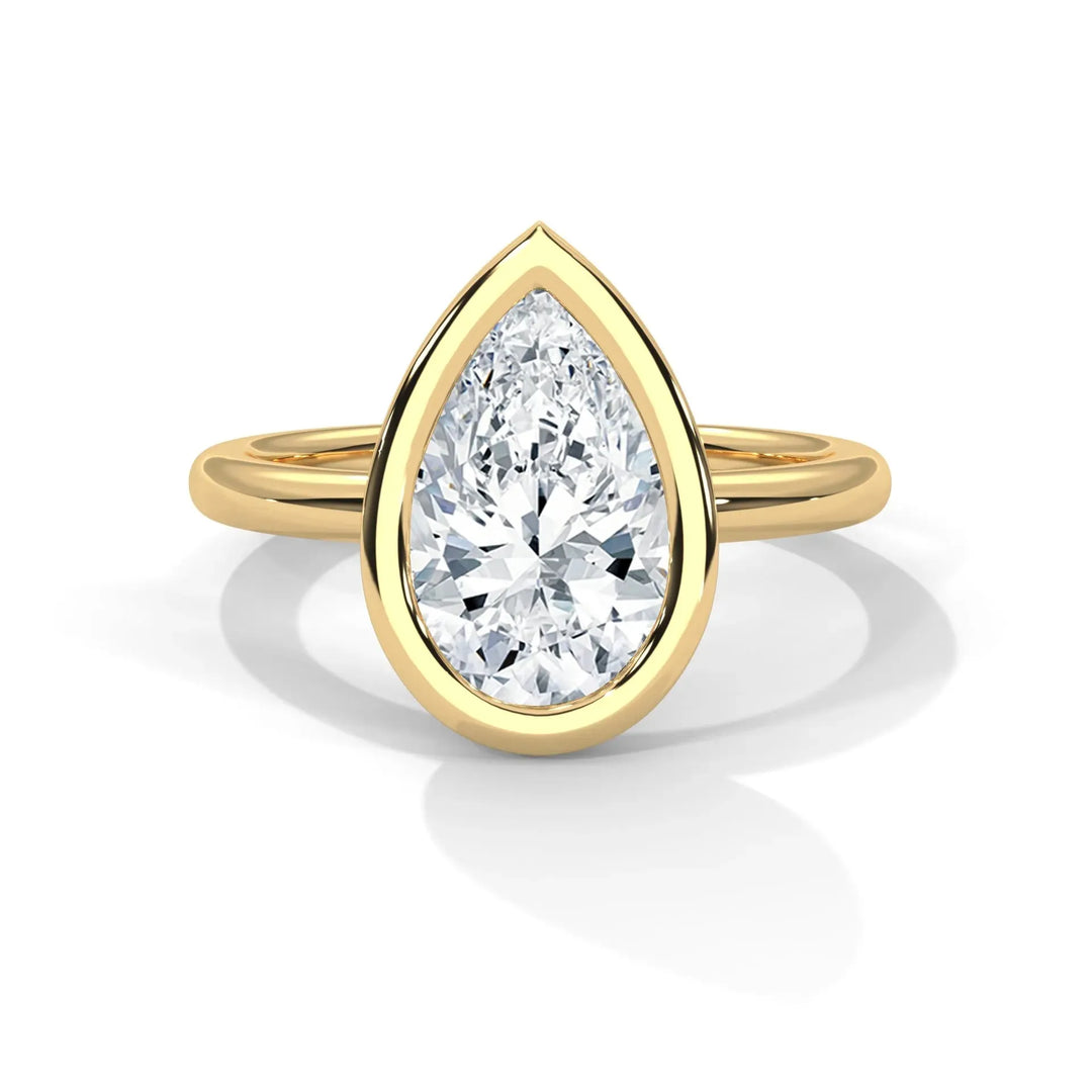 A gold ring with a prominent pear-shaped diamond set in a bezel. The design is elegant and luxurious, with a warm, sophisticated tone.