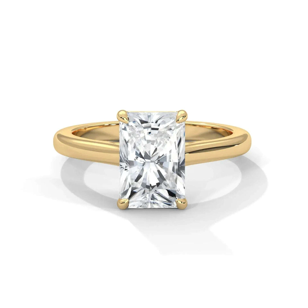 A gold ring with a radiant-cut diamond centerpiece set in four prongs, reflecting light brilliantly. The setting is simple, elegant, and sophisticated.