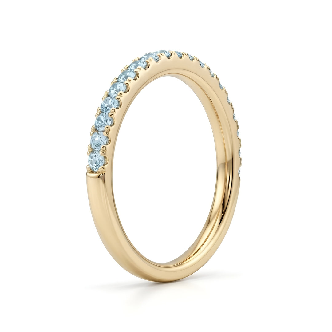 A gold ring with a thin band is adorned with sparkling blue gemstones along the top half, exuding elegance and simplicity against a white background.