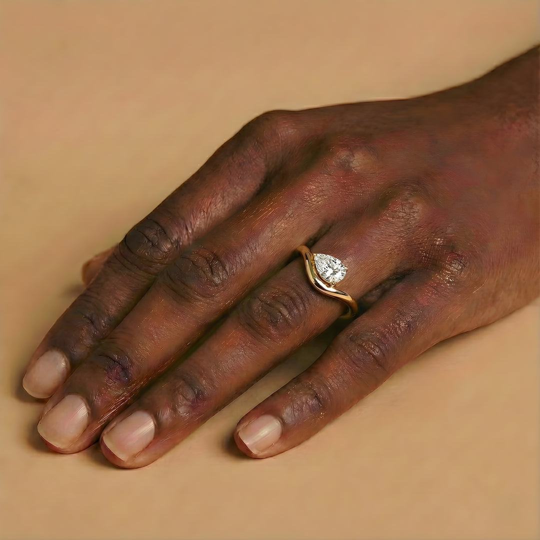 Hand wearing a gold ring with a diamond on a beige background