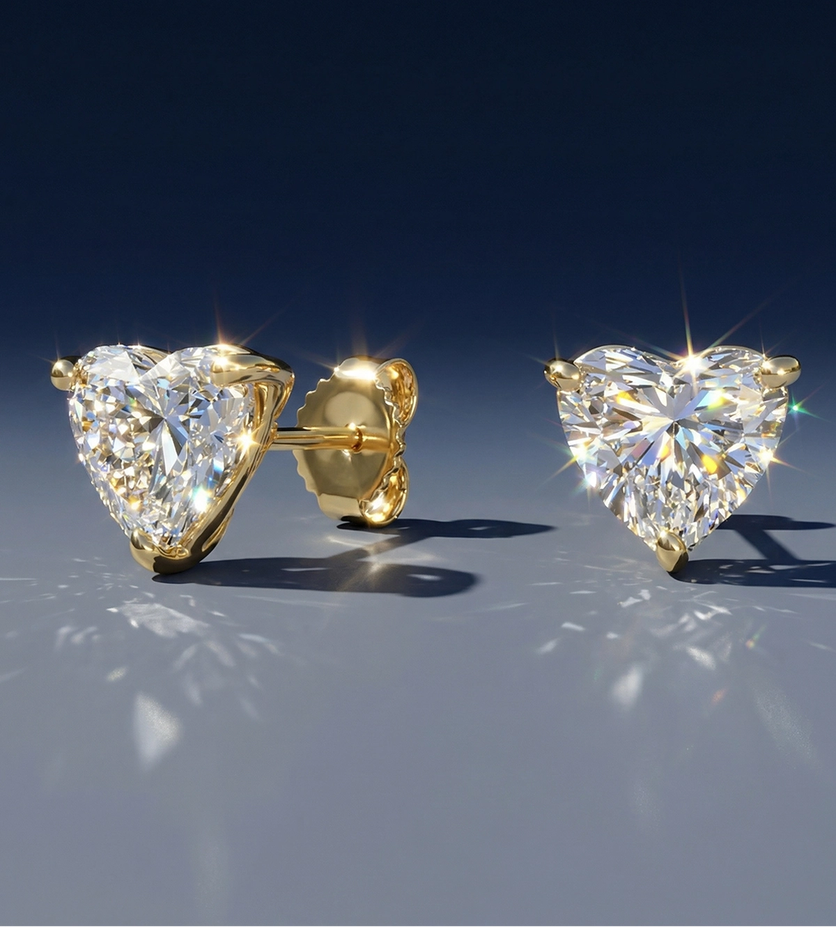 Brilliant heart-shaped diamond stud earrings set in polished yellow gold, showcasing exceptional sparkle and light reflection on a soft gray surface.
