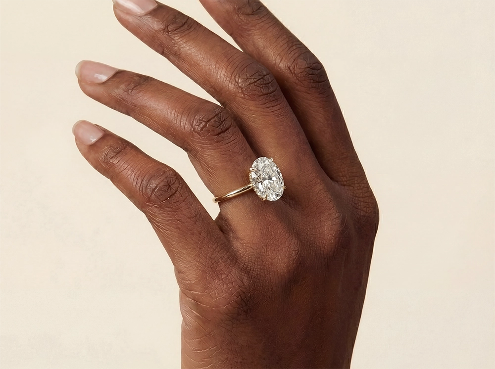 Elegant oval solitaire diamond engagement ring set in polished yellow gold worn on a hand, featuring a brilliant cut stone and minimalist design.