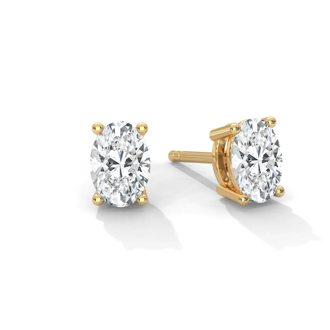 A pair of oval cut diamond earrings with gold settings on a white background.