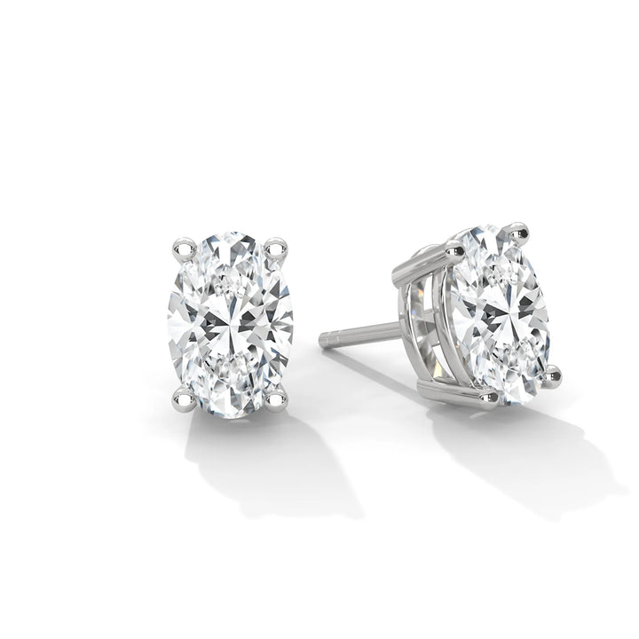 A pair of oval cut diamond stud earrings in a four prong setting on a white background.