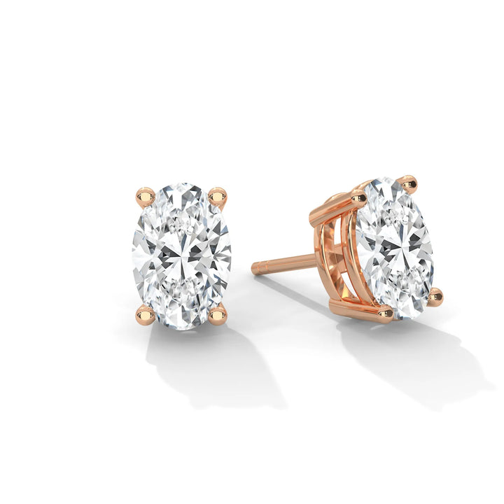 Pair of oval cut diamond stud earrings with rose gold settings on a white background.