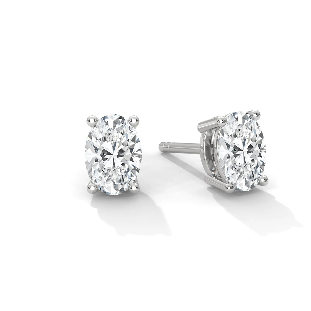 A pair of oval cut diamond stud earrings set in silver on a white background.