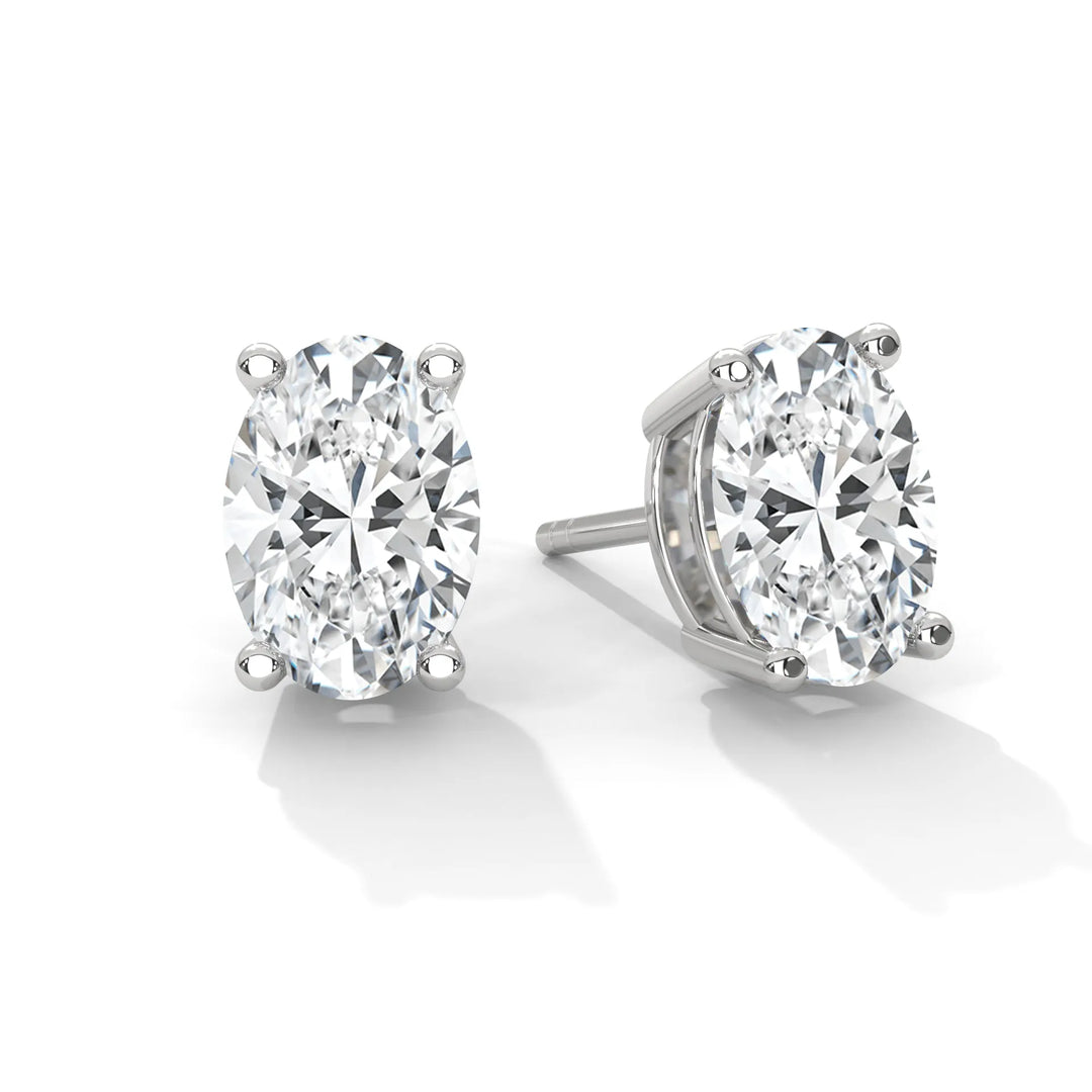 A pair of oval cut diamond stud earrings in a silver setting on a white background.