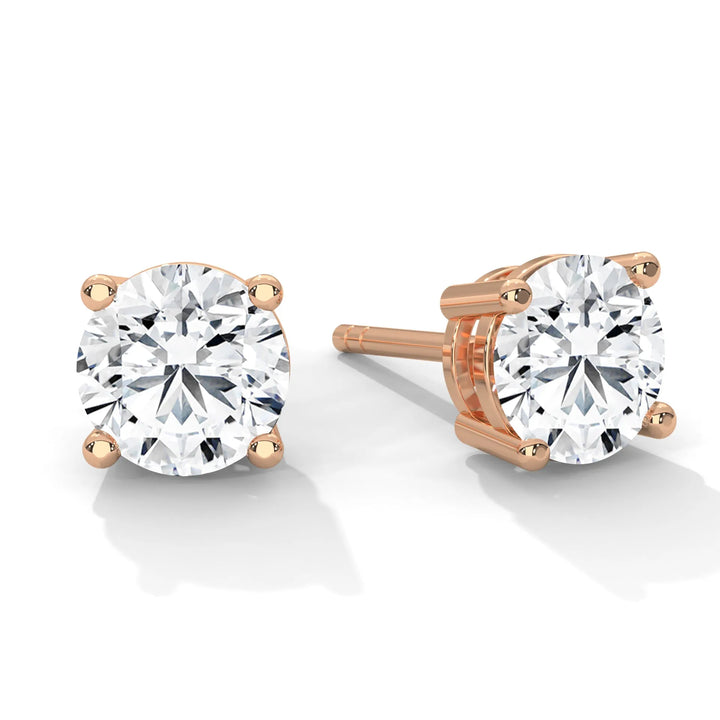 A pair of round cut diamond earrings with rose gold settings on a white background.