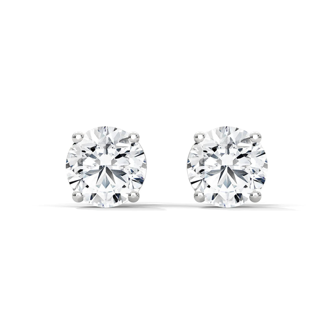 A pair of round cut diamond stud earrings in a four prong setting on a white background.