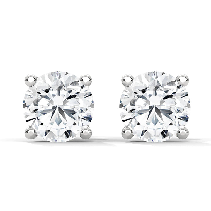 A pair of round cut diamond stud earrings with four prong settings on a white background.