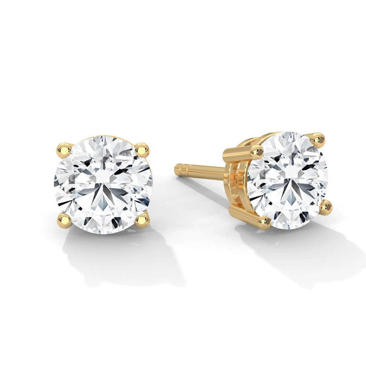 A pair of round cut diamond stud earrings with gold prongs on a white background.