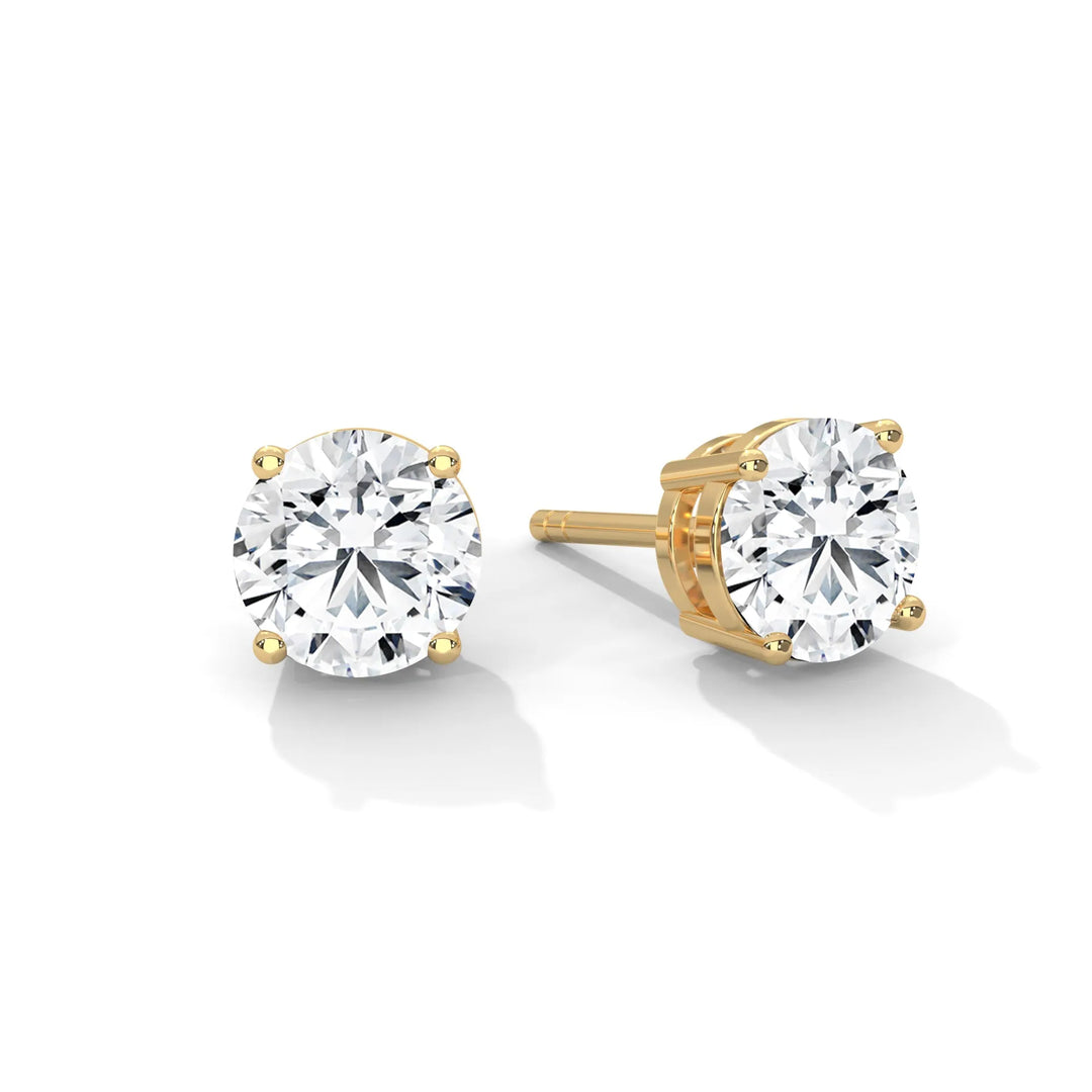 A pair of round cut diamond stud earrings set in gold on a white background.