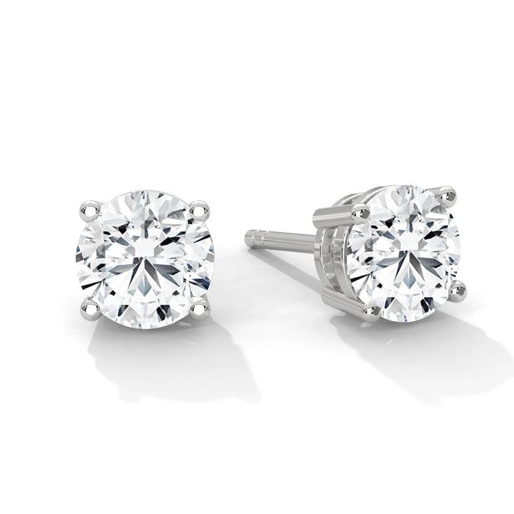 A pair of round cut diamond stud earrings set in silver prongs on a white background.