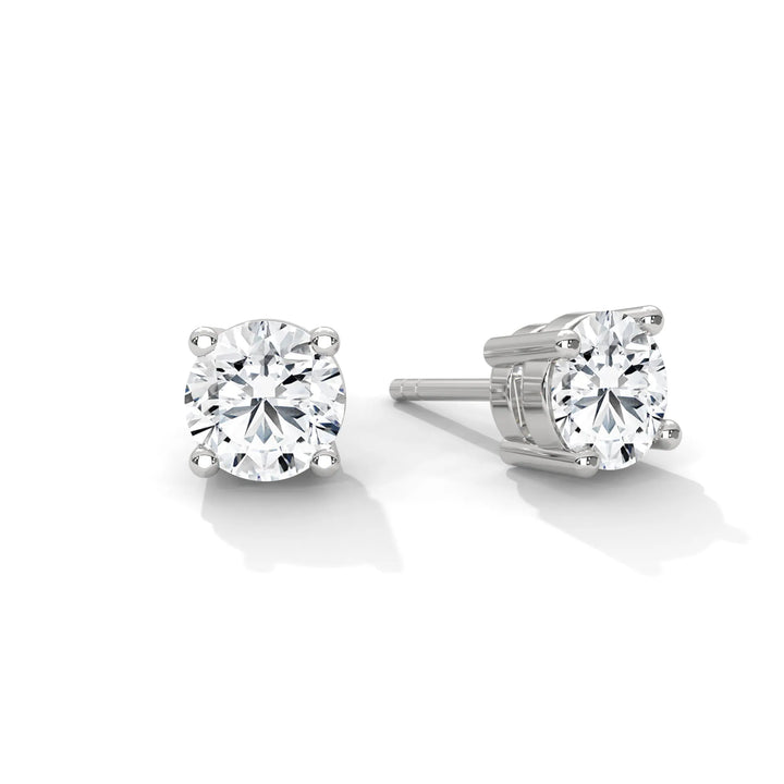 A pair of round cut diamond stud earrings with silver prong settings on a white background.