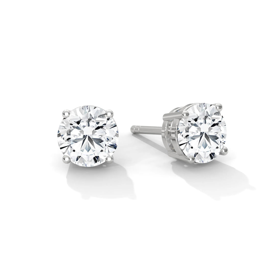 A pair of round cut diamond stud earrings in white gold settings on a white background.