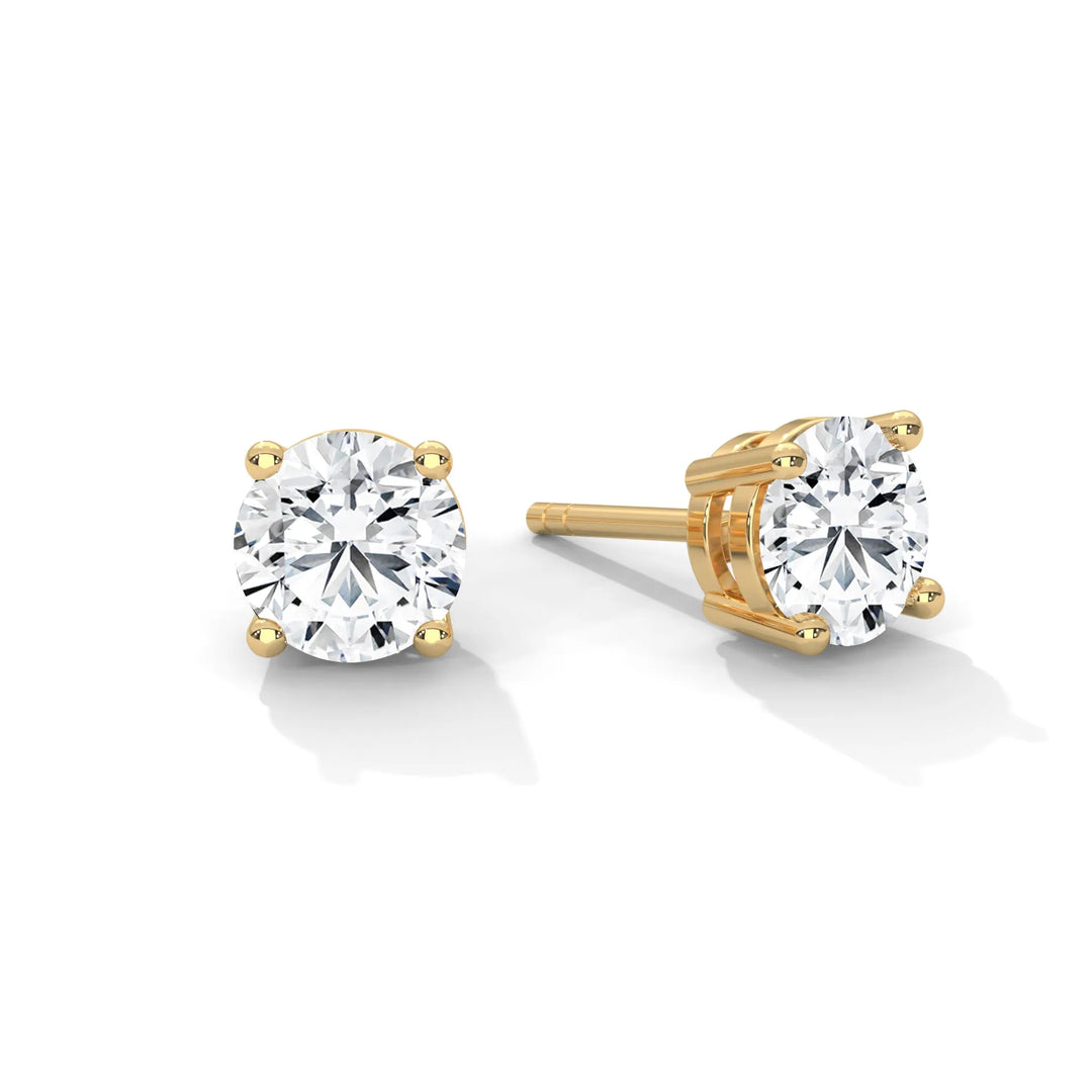 Pair of sparkling round cut diamond stud earrings in gold settings on a white background.