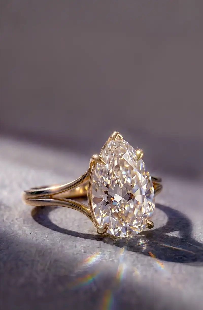 Vertical close-up of a gold solitaire engagement ring featuring a sparkling pear-cut diamond in natural light