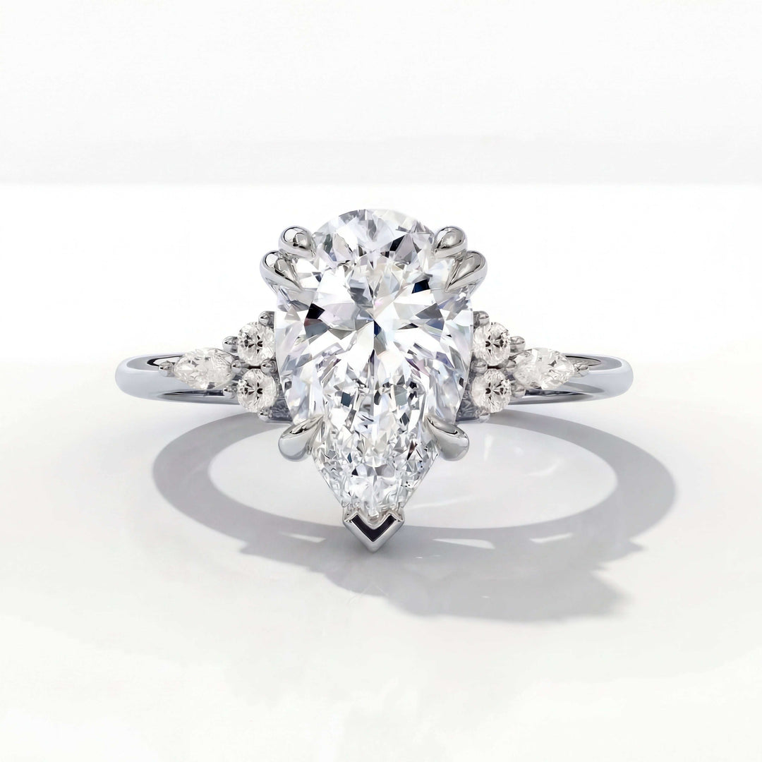 A pear-shaped diamond engagement ring with side stones set on a sleek, reflective white gold band, conveying elegance and sophistication.
