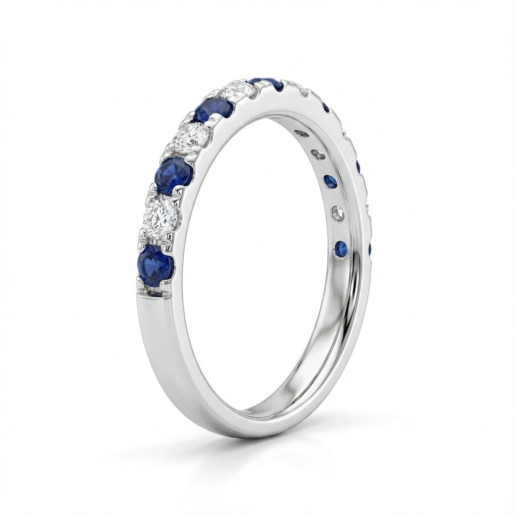 Silver ring with alternating blue sapphires and white diamonds, elegantly set in a pattern. The backdrop is plain white, highlighting its sparkle.