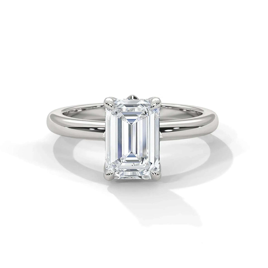 A solitaire engagement ring with an emerald-cut diamond set on a sleek, polished white gold band, exuding elegance and sophistication against a plain background.