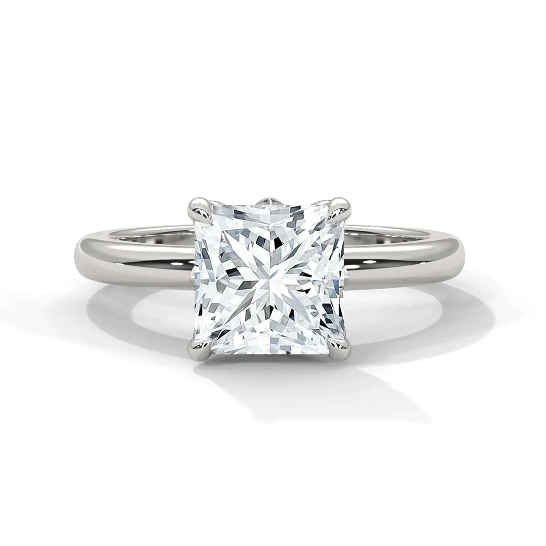A solitaire ring features a large, square-cut diamond in a four-prong setting on a sleek silver band, exuding elegance and simplicity.