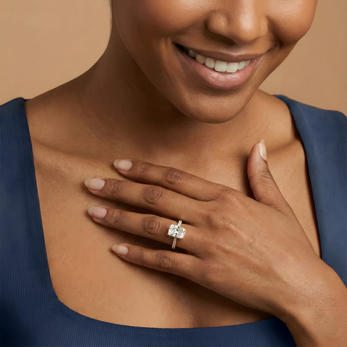 Woman wearing a diamond ring on her hand with a blue top against a beige background