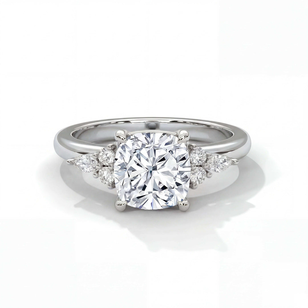 A sparkling engagement ring with a round diamond center stone flanked by smaller round and teardrop diamonds on a sleek silver band. Elegant and luxurious.